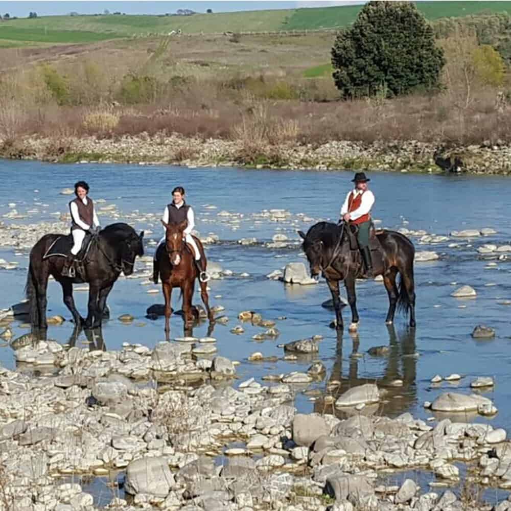 People on horseback fording the Orcia river in Tuscany